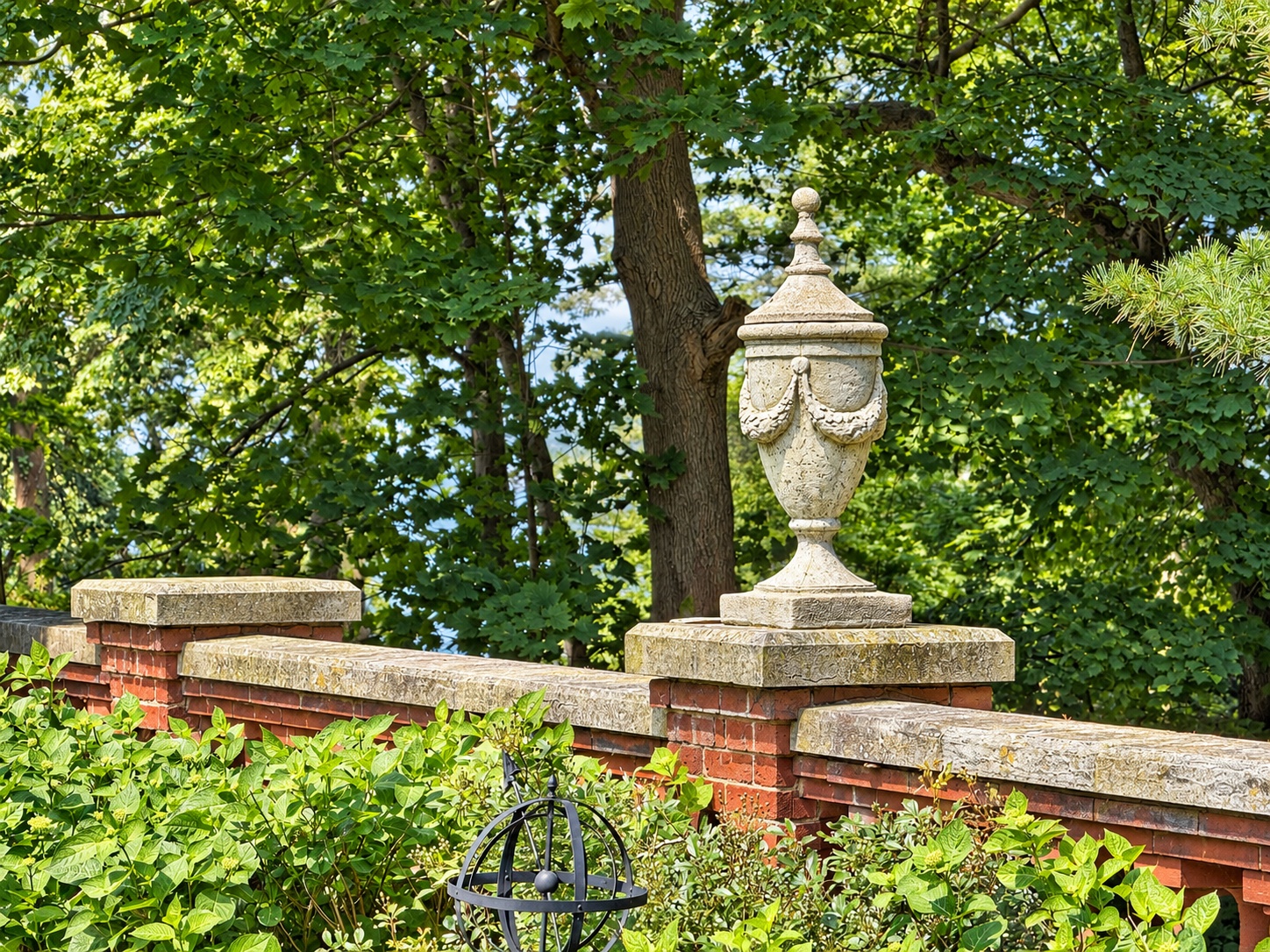 Decorative stone urn on a brick balustrade, framed by trees and greenery